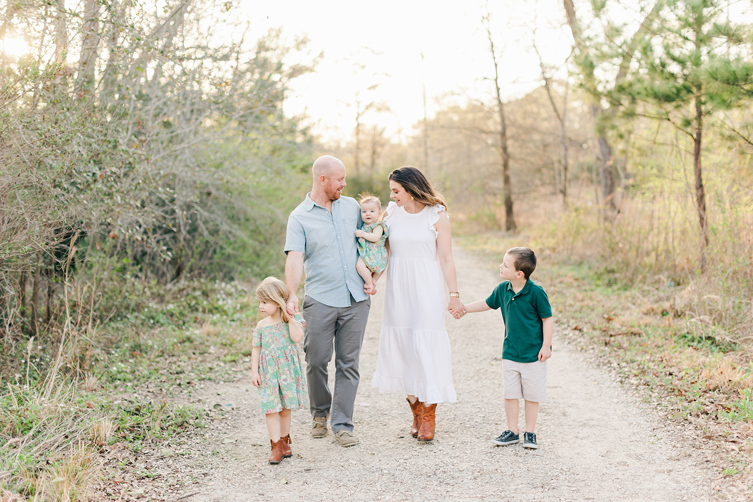 Family Photographer Monette Anne captures a beautiful photo of a young family holding hands on a road in Texas. family on the road young family neutral family photo outfits sunset photos #youngfamilyphotographertexas #familyphotoinspiration #texasphotographer #houstontexasphotography #familyphotographer #memorialparkhouston #houstontexasfamily photographer #monetteanne #monetteannephotography #texasfamilyphotographer #familyphotos #southernrootsphotography