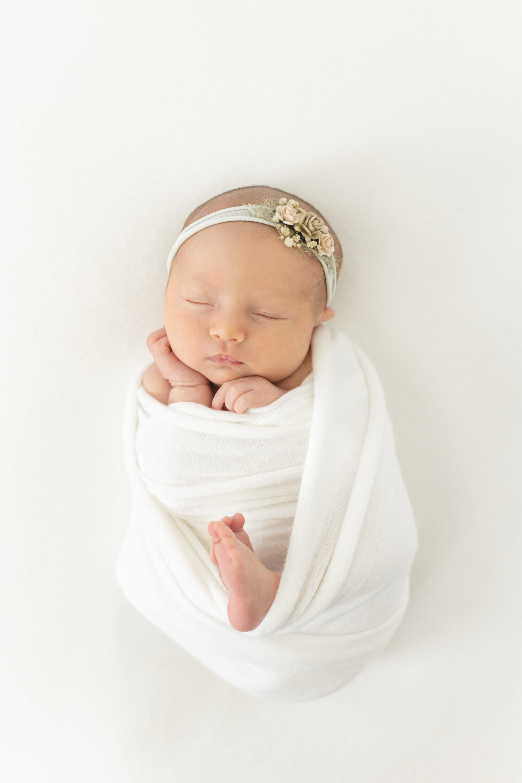 Houston, Texas newborn photographer, Monette Anne Photography captures this sleeping swaddled newborn during this at-home session. newborn session white muslin baby swaddle muslin white floral newborn headband sleeping newborn houston photographer #HoustonTexasNewbornPhotographer #HoustonTexasFamilyPhotographer #LifestyleNewbornSession #HoustonHeightsNewbornPhotographer #HoustonHeightsFamilyPhotographer #NewbornPhotos #MonetteAnnePhotography #LifestyleFamilyPhotoSession #NewbornOutfit #BabyGirl